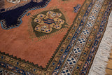 Pale gold and navy finned medallion on dusty sandalwood field, intricate border, fringe.