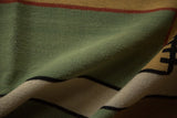 Detail of folded Contemporary Kilim rug with green, sand, and black geometric patterns.
