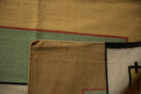 Hand woven Kilim rug corner displaying abstract geometric beige, green, and cinnabar red.