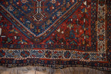 Corner of a vintage Shiraz rug with geometric borders, a sapphire blue medallion, and wool fringe.