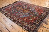 Angled view of a vintage Shiraz rug showcasing its sapphire blue and cherry red geometric diamond medallions.