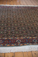 Intricate Herati motif on a green field, with a brick red border and ivory fringe.