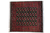 Vintage Pakistani Bokhara square carpet with geometric gul medallions in rust and ivory on a forest green field.