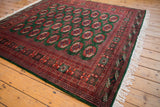 Vintage Pakistani Bokhara carpet from a high angle, showing the repeating gul medallions on a lustrous forest green field.