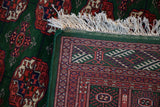 Corner of a Bokhara rug showing the hand-knotted back, green selvage, and full ivory fringe.