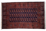 Vintage Pakistani Bokhara carpet with repeating rust gul medallions on a deep navy blue field.
