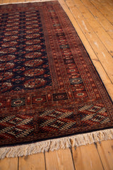 Angled view of a vintage Bokhara rug's intricate rust border and plush navy blue field.