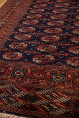 Angled detail showing the lustrous wool pile and Bokhara gul medallions in navy and rust.