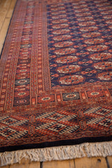 Angled view of a Bokhara carpet corner, highlighting the intricate rust border and plush navy pile.