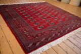 Plush cherry red Bokhara rug, showcasing intricate gul medallions and geometric borders.