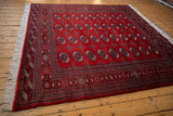 Cherry red Pakistani Bokhara rug corner showcasing ornate geometric borders and white fringe.
