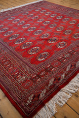 Cherry red Bokhara rug corner with detailed gul medallions, geometric borders, and white fringe.