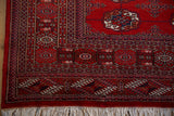 Cherry red Bokhara rug corner showing geometric gul motifs, navy borders, and white fringe.