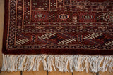 The maroon border and original secured ivory fringe on a vintage Bokhara carpet.