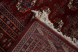 A folded corner of a vintage Bokhara rug showing its hand-knotted back and ivory fringe.