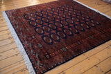 Lustrous wool pile of a vintage Pakistani Bokhara rug with red gul medallions on a dark navy field.
