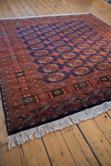 Angled corner view of a vintage Bokhara rug showing its plush pile, intricate border, and full fringe.