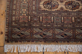 Vintage Bokhara rug corner with white fringe, detailed borders, camel and navy gul motifs.