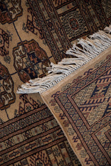 Tight, fine weave with secured fringe on a folded Pakistani Bokhara rug showing gul medallions in camel and navy.