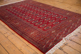 Angled view of a vintage Bokhara carpet showcasing the lustrous red pile and repeating gul medallions.