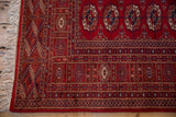 Detailed corner of a red Bokhara carpet showing intricate geometric borders and intact ivory fringe.