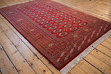 Vintage Pakistani Bokhara carpet's lustrous red pile and repeating gul pattern seen from an angle.
