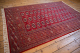 Full length view of a vintage Bokhara carpet highlighting its lustrous cherry red pile and geometric pattern.