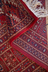 Plush cherry-red pile and intact ivory fringe of a fine hand-knotted Bokhara design carpet.
