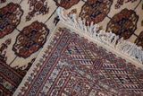 Corner of a vintage Bokhara carpet showing the plush wool pile and intact white fringe.