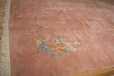 Close-up on the sprawling foliage and plush dusty rose pile of a vintage Art Deco carpet.