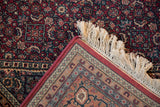 Corner detail of vintage Indian Bijar rug: raspberry Herati pattern, woven border, ivory fringe.