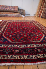 Low angle on a vintage Engelas rug's dense cherry red pile and navy Herati design.