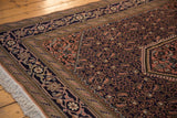 Close-up of the vintage Ardebil rug's apricot Herati field, navy floral border, and white fringe.