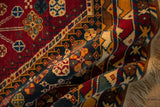 Folded Indian Shiraz design carpet with cherry red, navy blue vinery, full pile, and fringe.