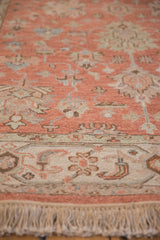 Detail of dusty rose field, ivory border with slate blue floral patterns, and fringe.