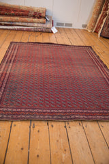 Angled view of a vintage Beljic rug, showcasing the intricate repeating floral gul motif in red and charcoal.