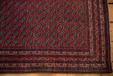 Corner view of a vintage Beljic rug showing its repeating floral gul motif and meandering vine border.