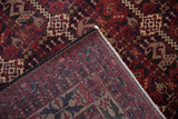 Hand-knotted Pakistani Belouch rug corner revealing cherry red geometric pile and woven foundation.