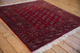 Angled view of a cherry red Pakistani Bokhara rug with repeating gul medallions and a lustrous pile.