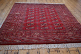 Traditional layout of a cherry red Pakistani Bokhara rug with repeating guls, viewed from an angle.