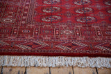 Detailed geometric border and plush ivory fringe of a vintage cherry red Bokhara rug.