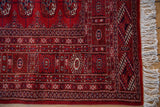 A detailed corner view of the vintage Bokhara rug's intricate red border and original ivory fringe.