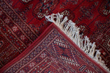Folded corner of a vintage Bokhara rug showing the fine weave, detailed border, and plush cherry red pile.