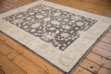 Angled perspective on a Peshawar rug's charcoal field with dense ivory floral vinery and wide border.