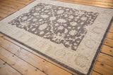 Peshawar rug from an angle, showing the charcoal floral field and wide ivory border.
