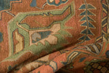 Folded vintage Soumac rug close-up: geometric serrated leaf motif in terra cotta, green, teal.
