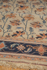 Vintage Soumac carpet close-up: terra cotta floral pattern, navy border, and light-colored fringe.