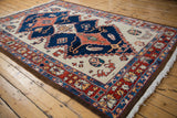 Detail of a vintage Northwest Persian rug, showing elongated navy and rust medallions with floral motifs on an abrashed ivory field.
