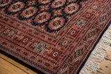 Geometric terra cotta, charcoal gul patterns on a Bokhara rug corner with ivory fringe.