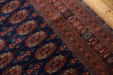 High sheen on the dense navy wool pile of a vintage Bokhara rug with rust and ivory gul medallions.
